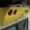 A yellow 1974-1982 REAR BUMPER - CHROME BUMPER LOOK tail light hangs from the side of a building.