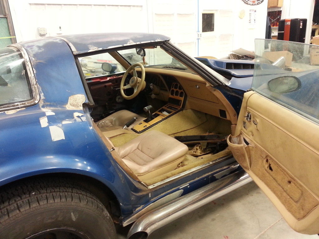 A blue corvette with its door open in a garage.