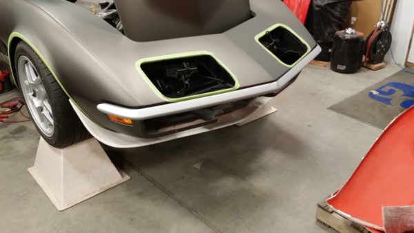 A gray 1968-1972 FRONT SPOILER - SS with a green hood is in a garage.