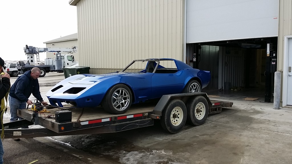 A blue corvette is being loaded onto a flatbed truck.