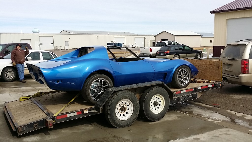 A blue corvette sports car on the back of a flatbed truck.