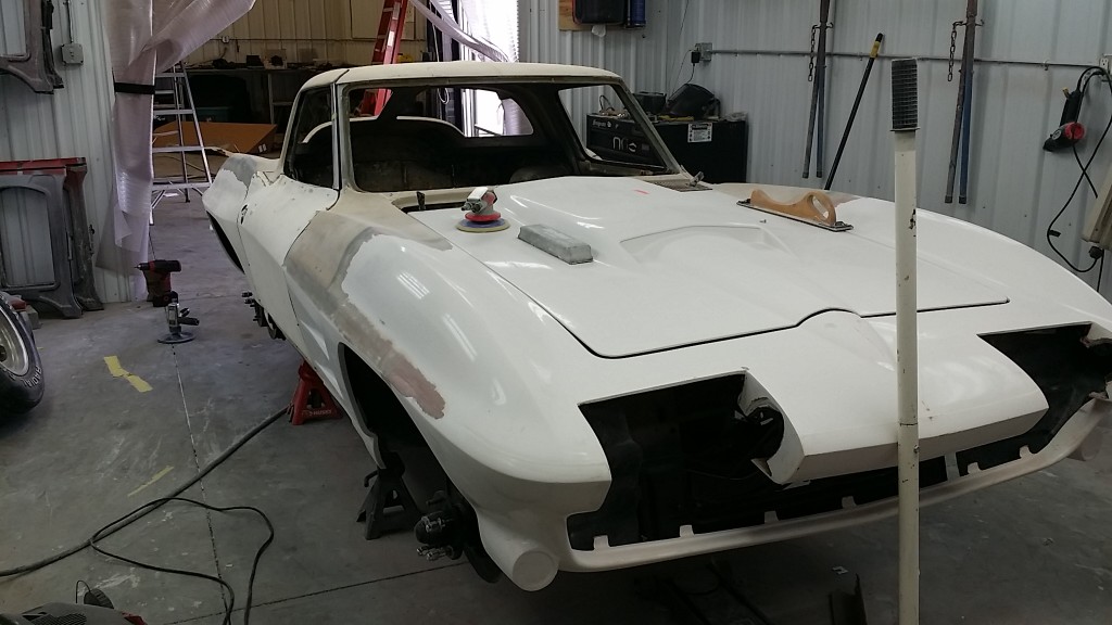 A white corvette is being worked on in a garage.