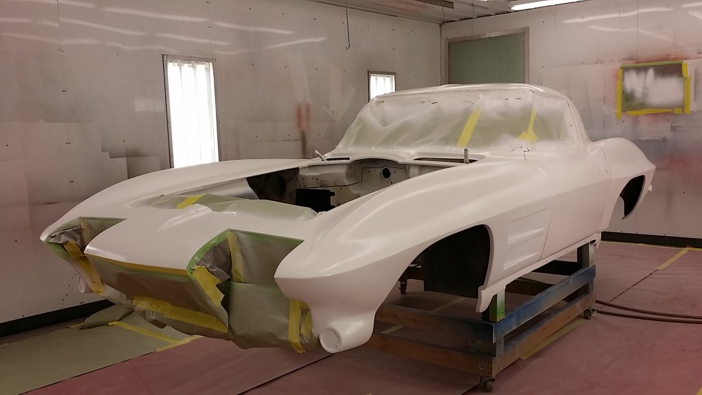 A white car is being painted in a garage.