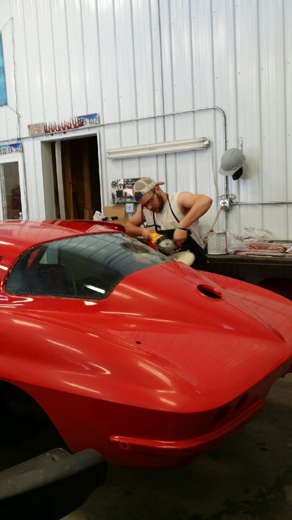 A man is working on a red car in a garage.