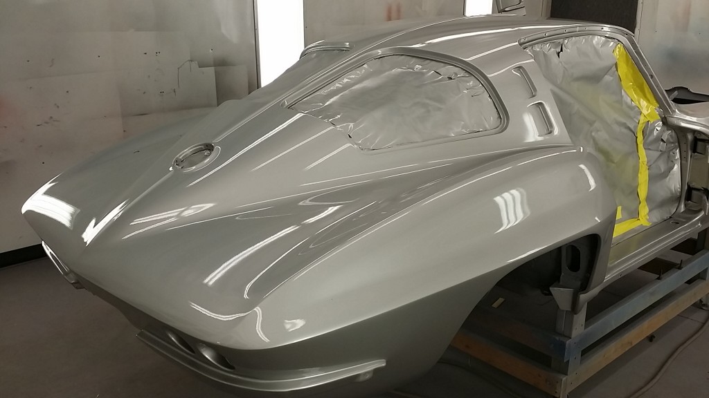A silver sports car is being painted in a garage.