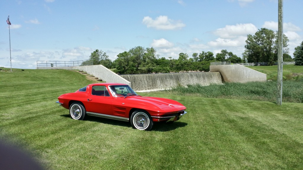 A red chevrolet corvette parked on a grassy field.