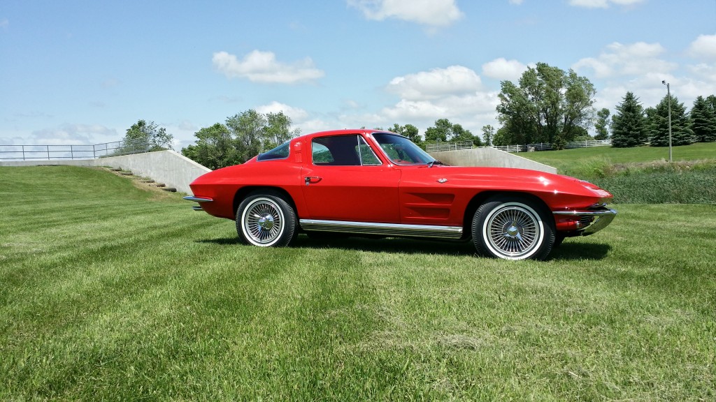 A red chevrolet corvette parked on a grassy field.