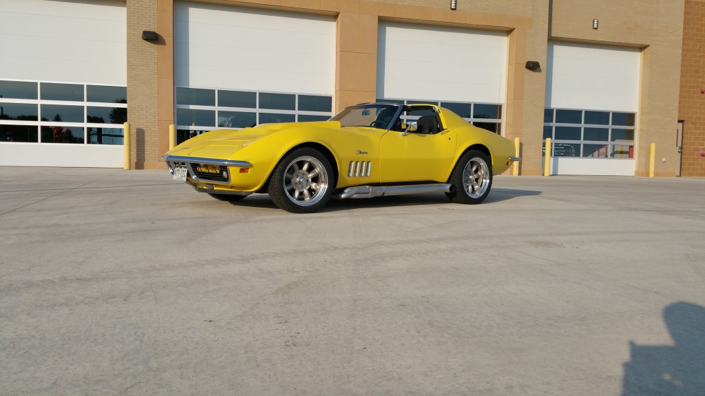 A yellow corvette parked in front of a garage.