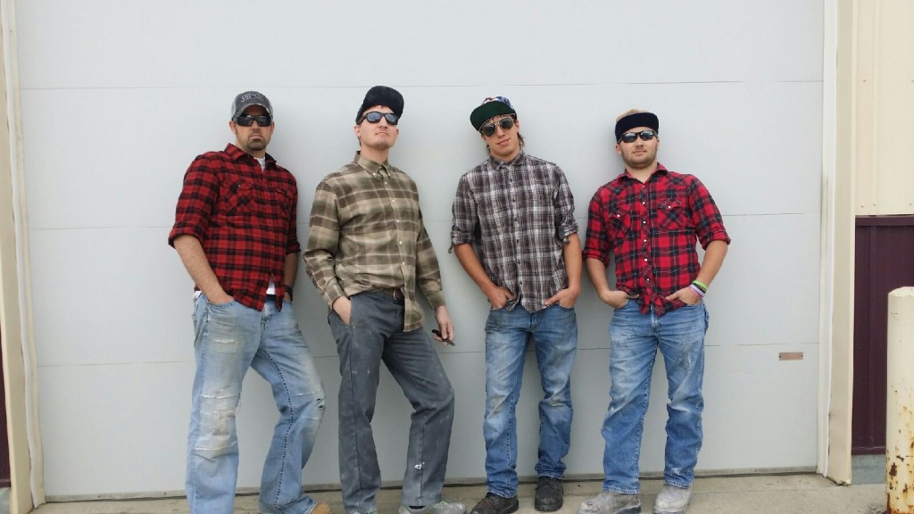 Four men in plaid shirts standing in front of a garage.
