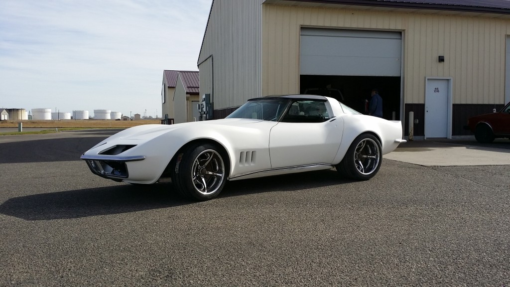 A white corvette parked in front of a garage.