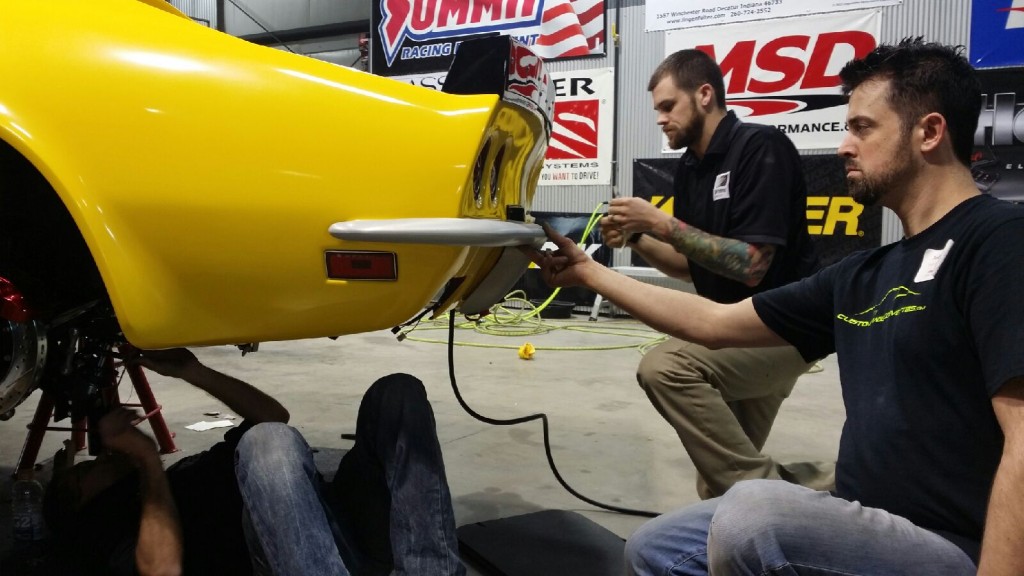 Two men working on a yellow car in a garage.