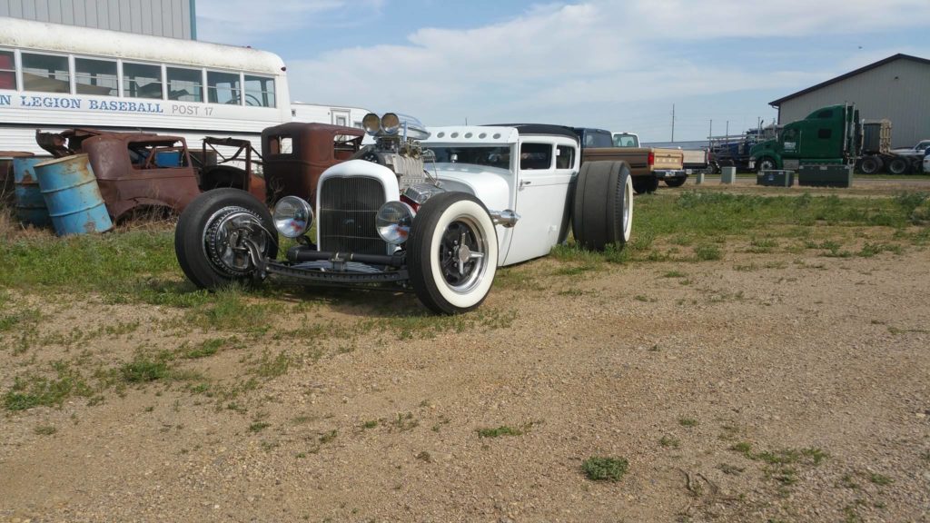 A white hot rod is parked in a dirt lot.