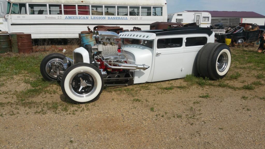 A white hot rod is parked in the dirt.