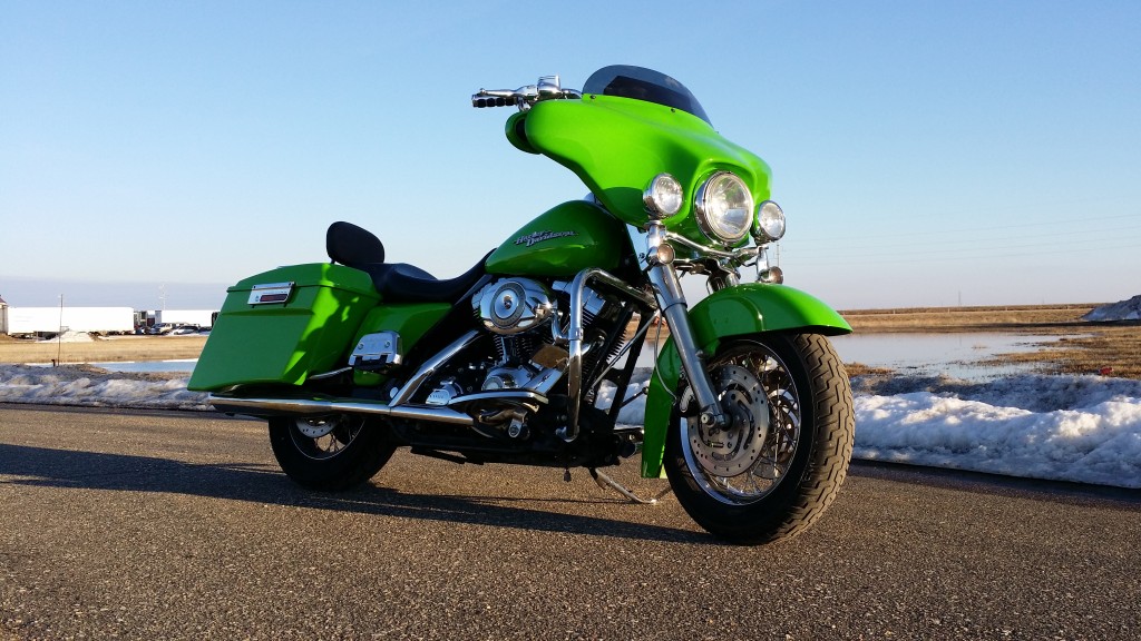 A green motorcycle is parked on the side of the road.
