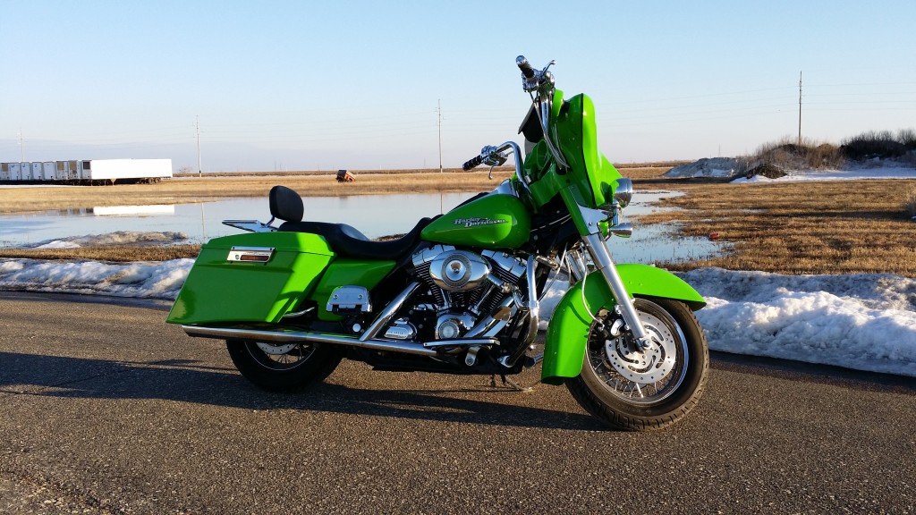 A green motorcycle is parked on the side of a road.
