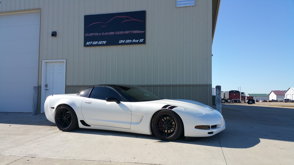 A white chevrolet corvette parked in front of a building.