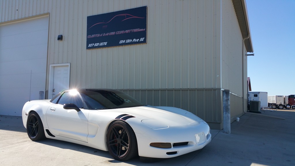 A white chevrolet corvette parked in front of a building.