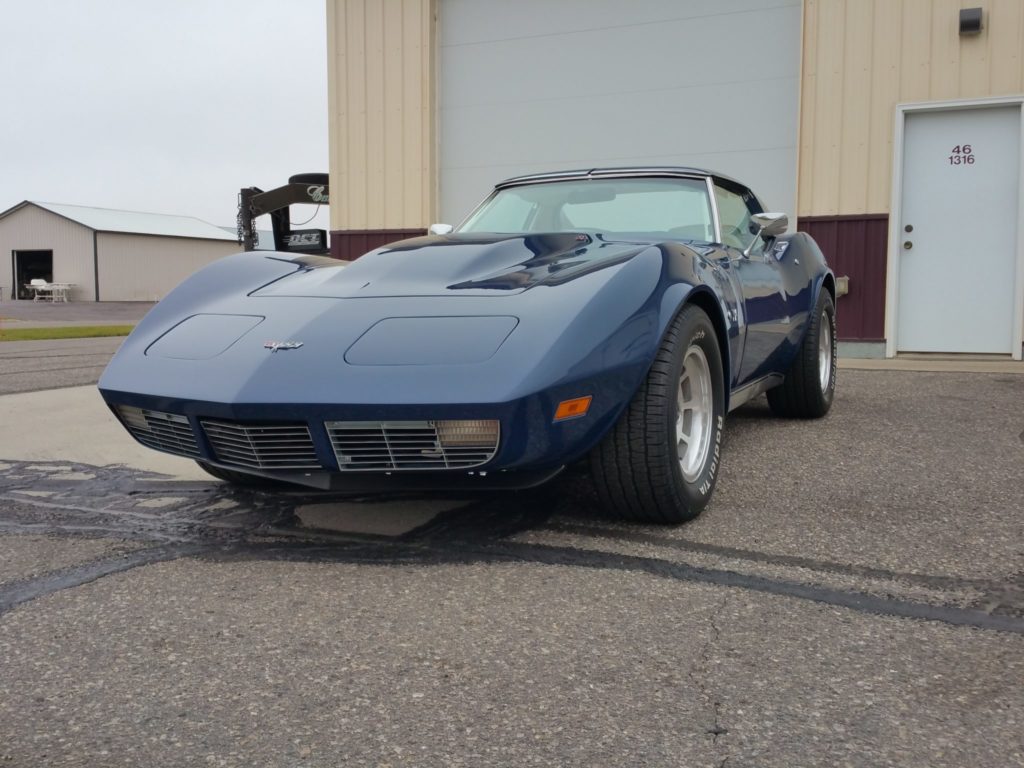A blue chevrolet corvette parked in front of a garage.