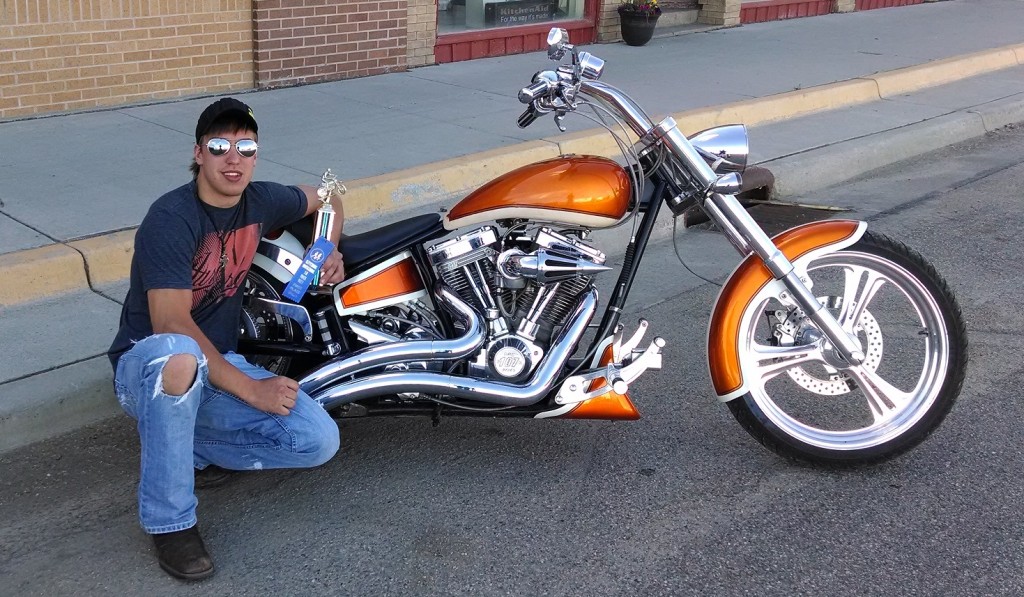A man posing next to a motorcycle with a trophy.