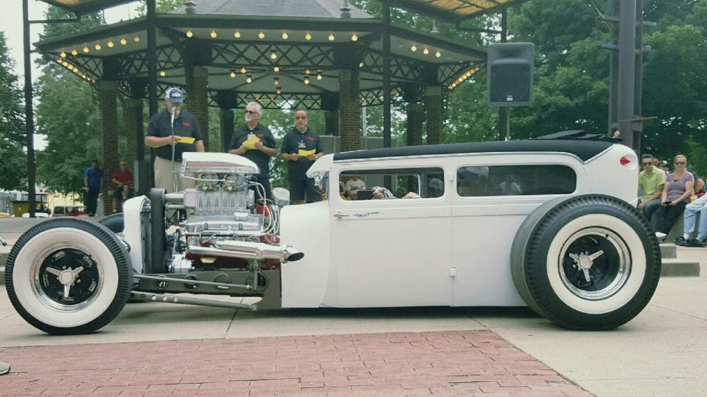 A white hot rod car is parked in front of a gazebo.