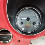 The dashboard of a red car with a DAKOTA DIGITAL HDX 3-1 GAUGES and clock.