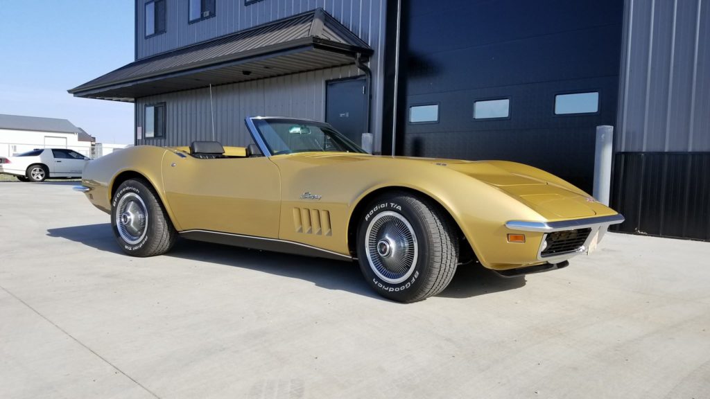 A yellow corvette parked in front of a garage.