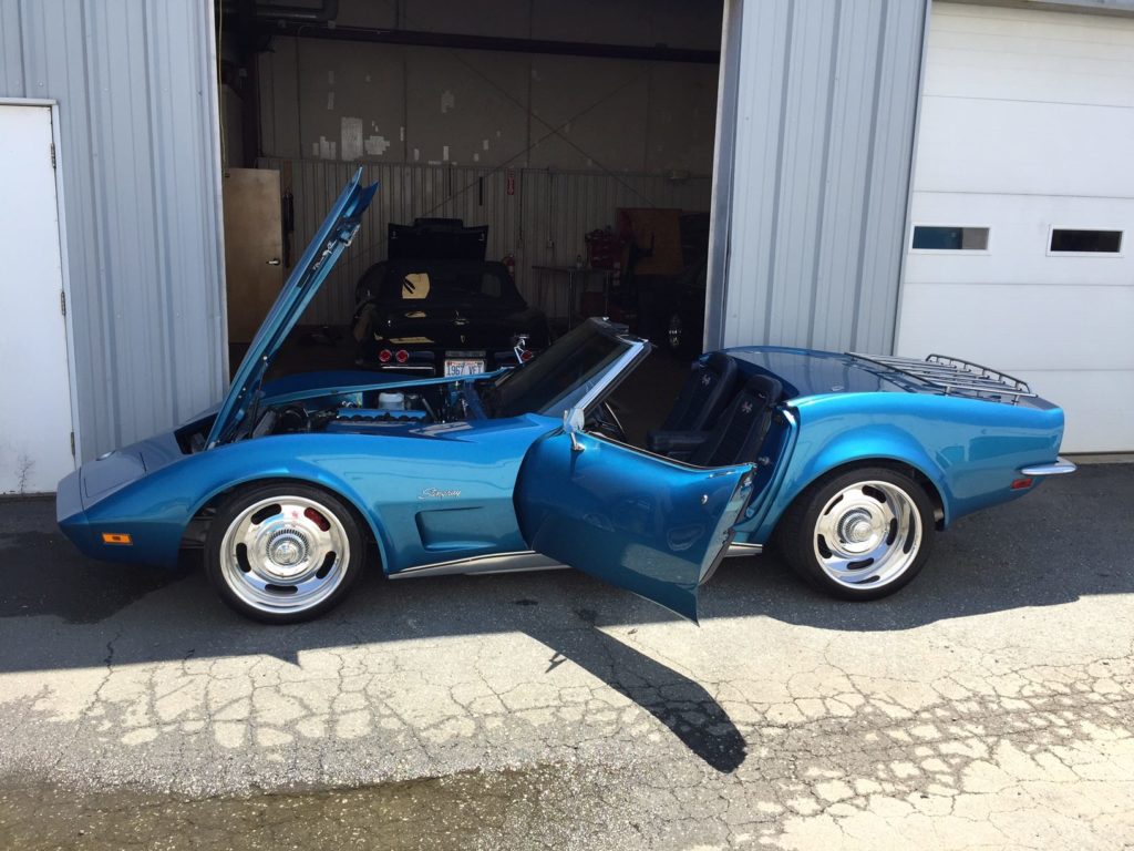 deep blue corvette in the shade with hood and doors open