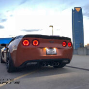 A 2005-2013 C6 Corvette parked on a rooftop with city skyscrapers in the background at dusk.