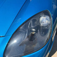 A close up of the 2005-2013 C6 CORVETTE CARBON FIBER HEADLIGHT BEZELS of a blue sports car.