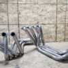 C2/C3 CORVETTE LS SWAP STAINLESS STEEL SIDE EXIT HEADERS - MILL FINISH on a concrete floor against a wall with osb panels.