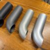 Four different types of C2/C3 CORVETTE LS SWAP STAINLESS STEEL SIDE EXIT HEADERS - CERAMIC FINISH on a wooden table.