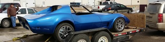 A blue corvette sports car on the back of a flatbed truck.