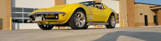 A yellow corvette parked in front of a garage.