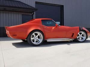 A red chevrolet corvette parked in front of a garage.